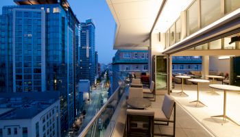 A modern outdoor terrace with seating overlooks a cityscape with tall buildings at dusk, featuring a mix of office and residential spaces.