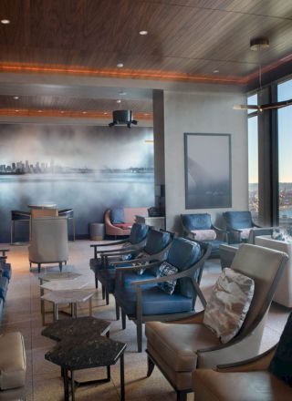 A modern lounge with comfortable seating, large windows offering a scenic view of water and a Ferris wheel, and a cityscape wall mural.