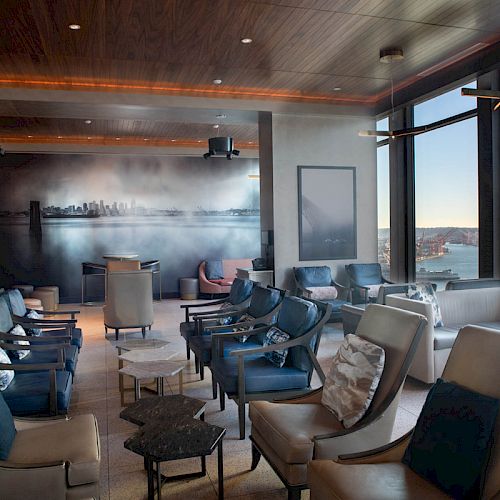 The image shows a modern lounge with numerous seats, large windows, and a cityscape mural on the far wall. A Ferris wheel is visible outside.