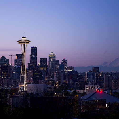 The image shows the Seattle skyline at dusk, featuring the Space Needle, tall buildings, and Mount Rainier in the background.