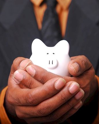 A person in a suit is holding a small white piggy bank in their cupped hands, symbolizing financial savings and care.